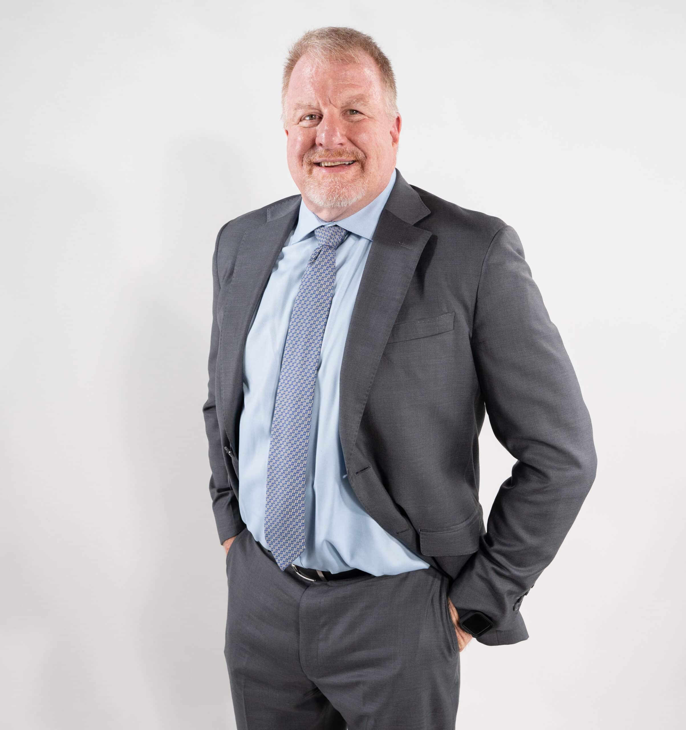 Dan B. Dalton, owner of P3:14 Consulting, stands confidently in a gray suit with a light blue shirt and patterned tie, smiling in front of a white background.